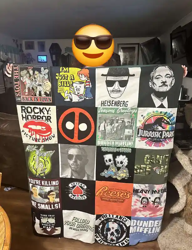 A person holds up a large quilt made from repurposed t-shirts featuring various pop culture references like Heisenberg…
