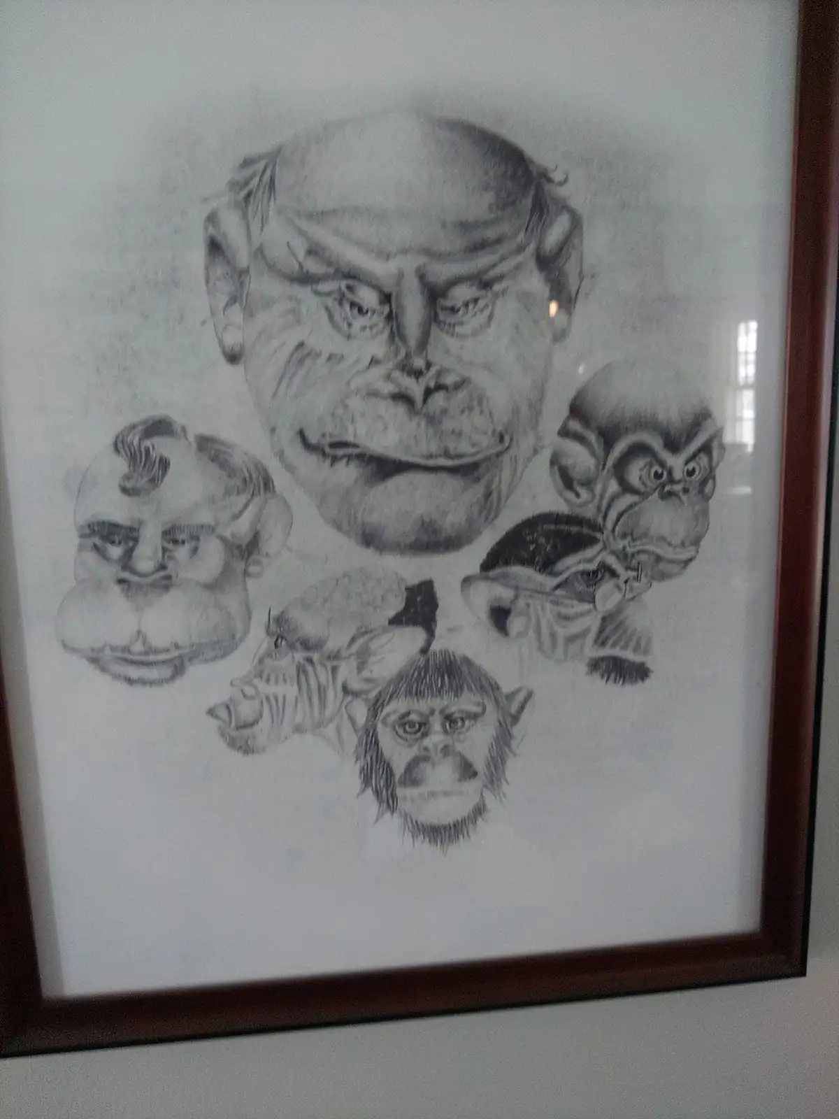 A framed pencil drawing shows a large, angry-looking human face at the top, surrounded by five smaller, grotesque…
