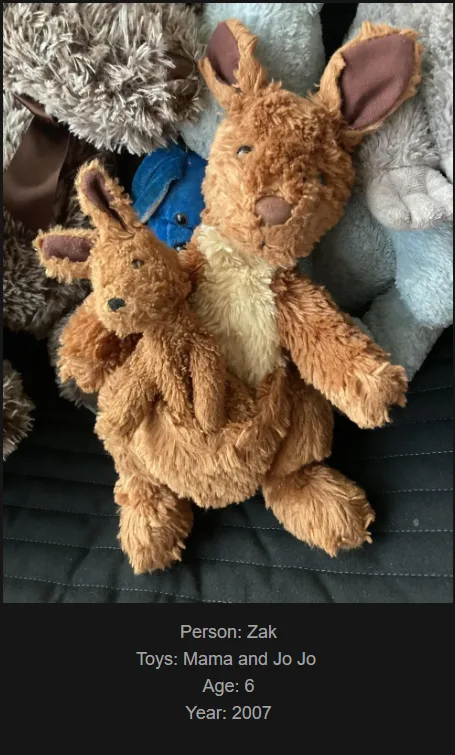 A photo of two brown stuffed kangaroos, one larger and one smaller, nestled together among other plush toys on a dark fabric…
