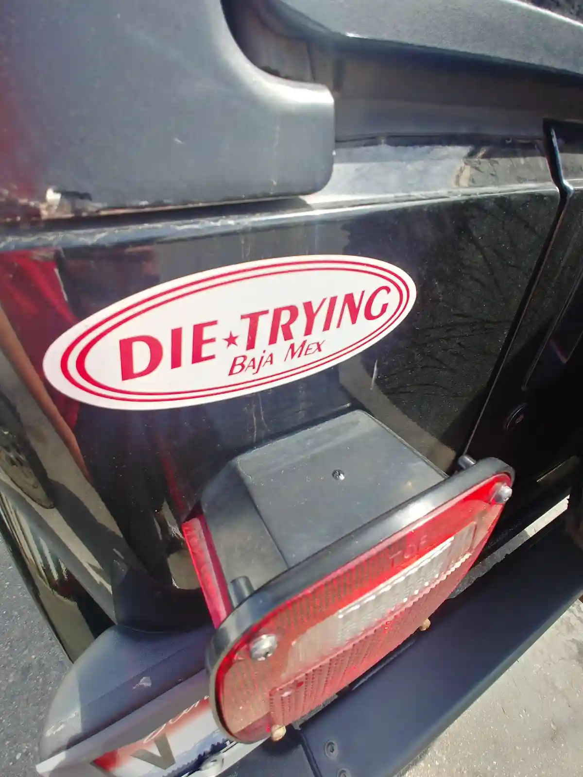 A close-up photo shows a red and white oval sticker on the glossy black rear fender of a vehicle, positioned above a red…