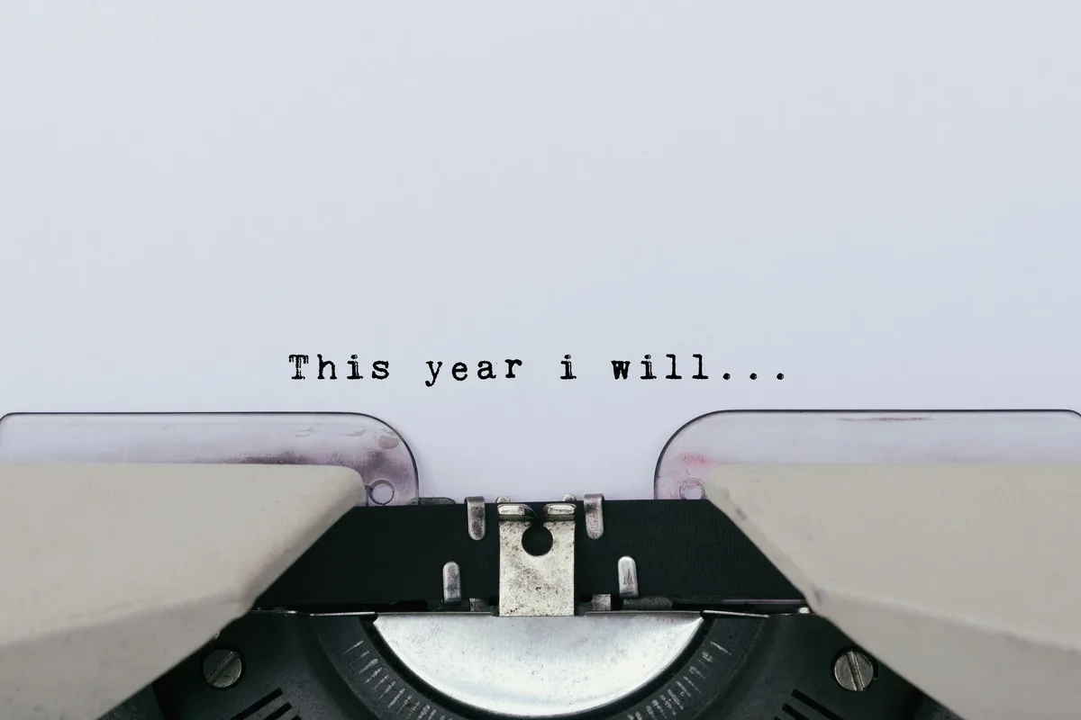 A close-up shot of a vintage typewriter poised over a blank sheet of paper, with the typed phrase 'This year i will...'…