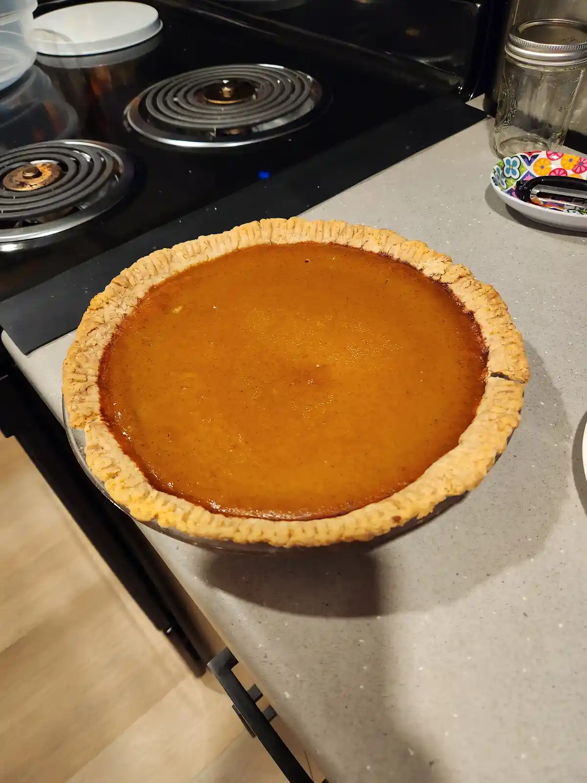 A freshly baked pumpkin pie sits on a kitchen counter next to a black electric stove. The pie has a golden-brown crust and…