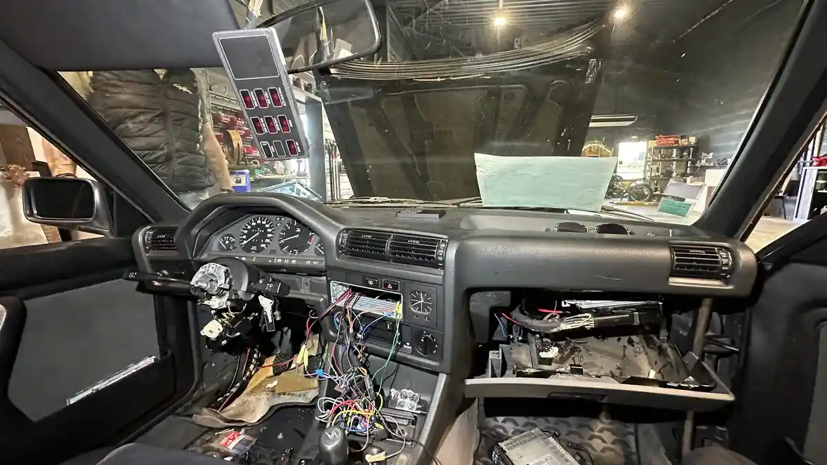 The image shows the interior of a car with its dashboard completely dismantled, exposing tangled wires, missing components…