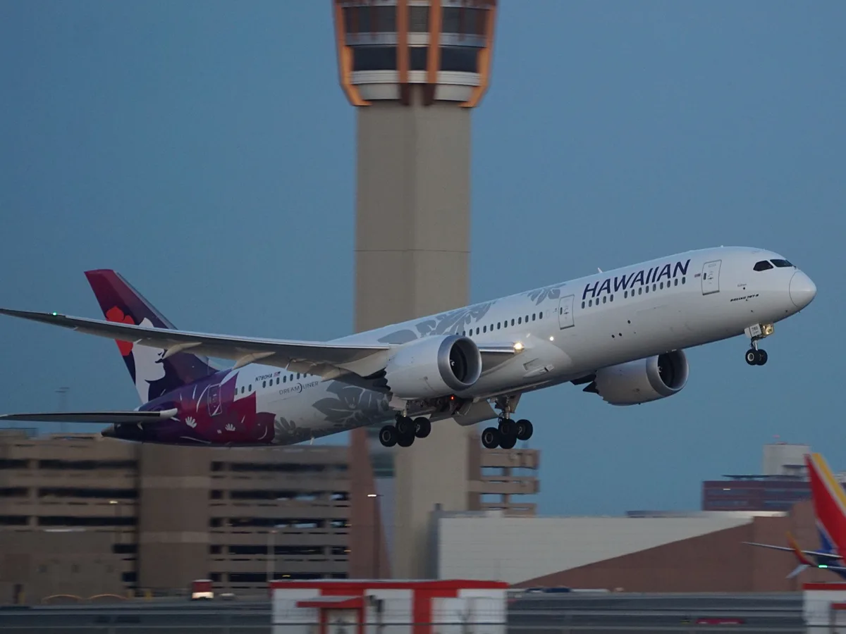 A Hawaiian Airlines Boeing 787 Dreamliner is captured mid-air during takeoff, with its landing gear still extended. The…