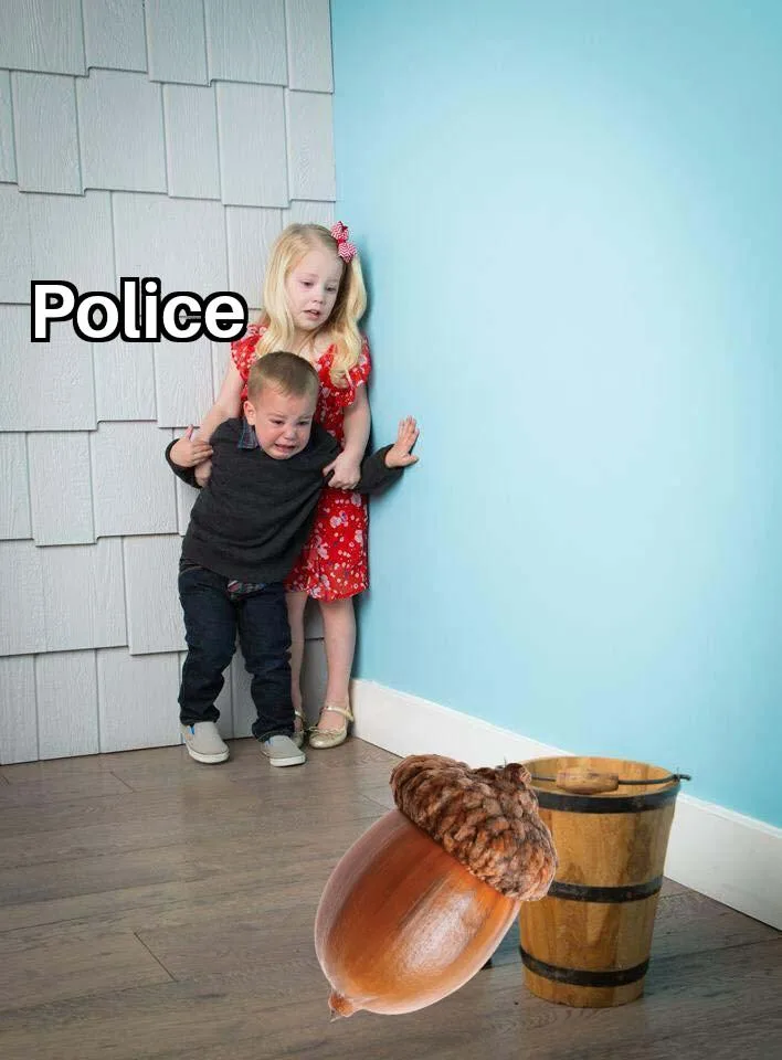 Two young children, a girl in a red dress and a boy in a dark shirt, are hiding in a corner of a room with white shingled…