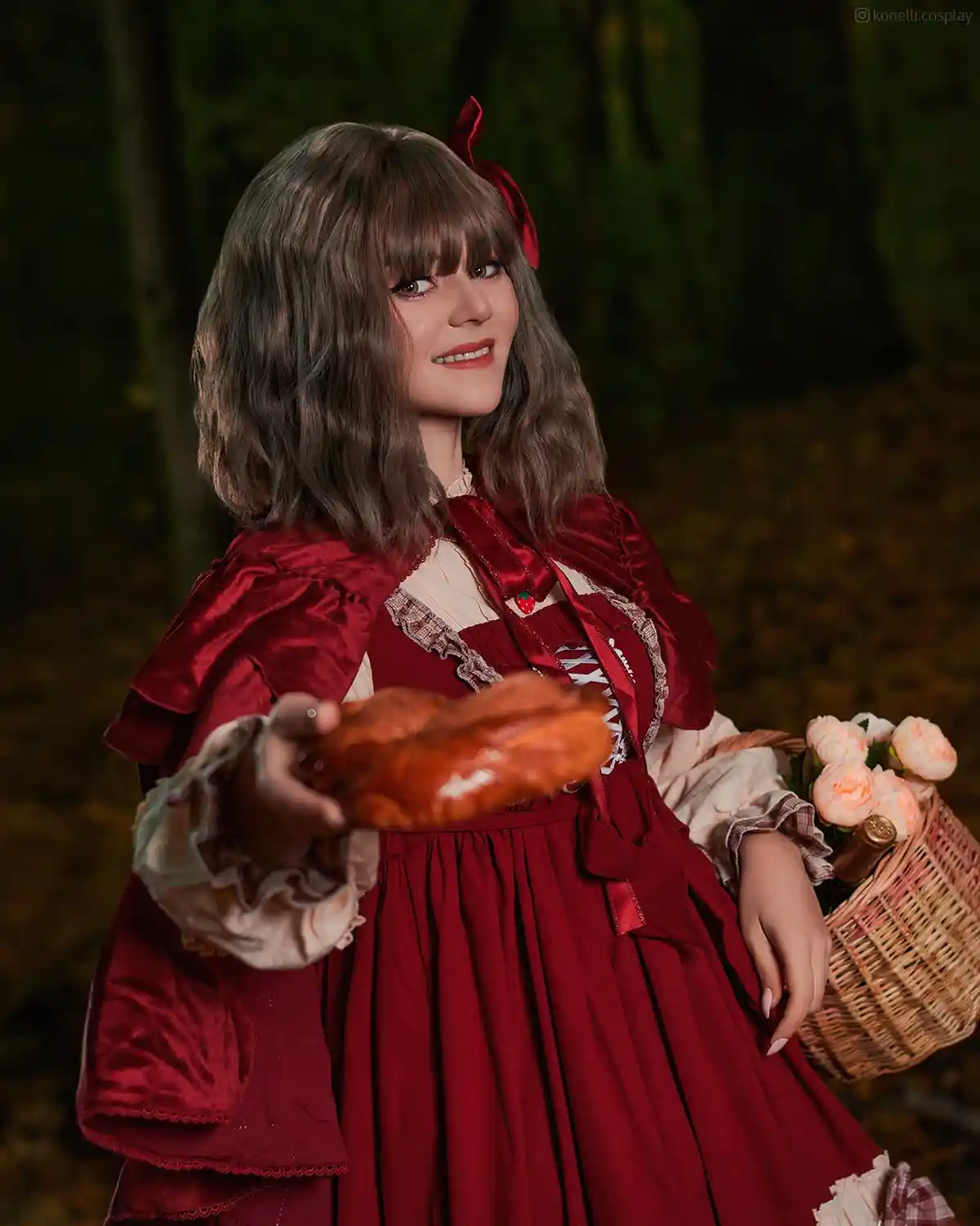 A person in a detailed red Little Red Riding Hood costume stands in a forest, holding out a loaf of bread toward the viewer…
