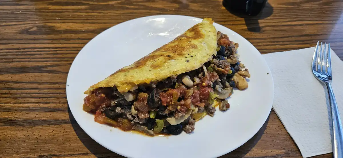 A plate of food on a wooden table, featuring a folded, golden-brown egg dish filled with a colorful mixture of ground meat…