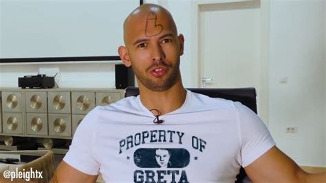 A bald man with a 'B' drawn on his forehead sits in a chair wearing a white t-shirt that reads 'PROPERTY OF GRETA' with a…