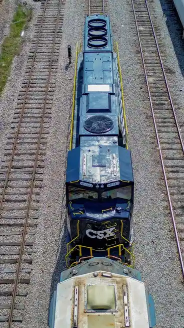 An aerial view shows a CSX locomotive, number 911343, on a railway track, with another train car partially visible below it…