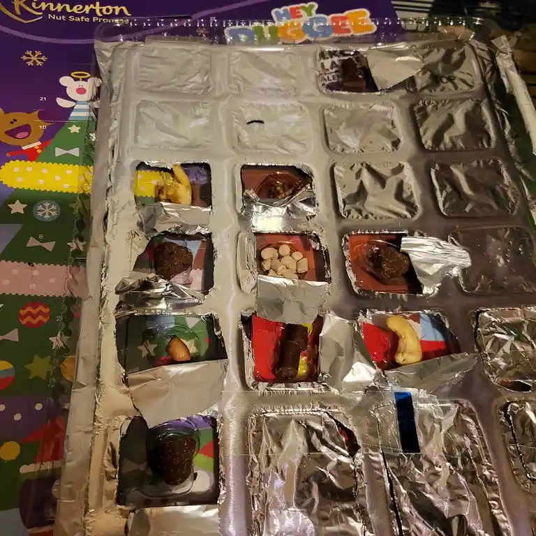 An open Rinnerton 'Hey Digg ee' chocolate advent calendar with many foil compartments torn open, revealing various chocolate…