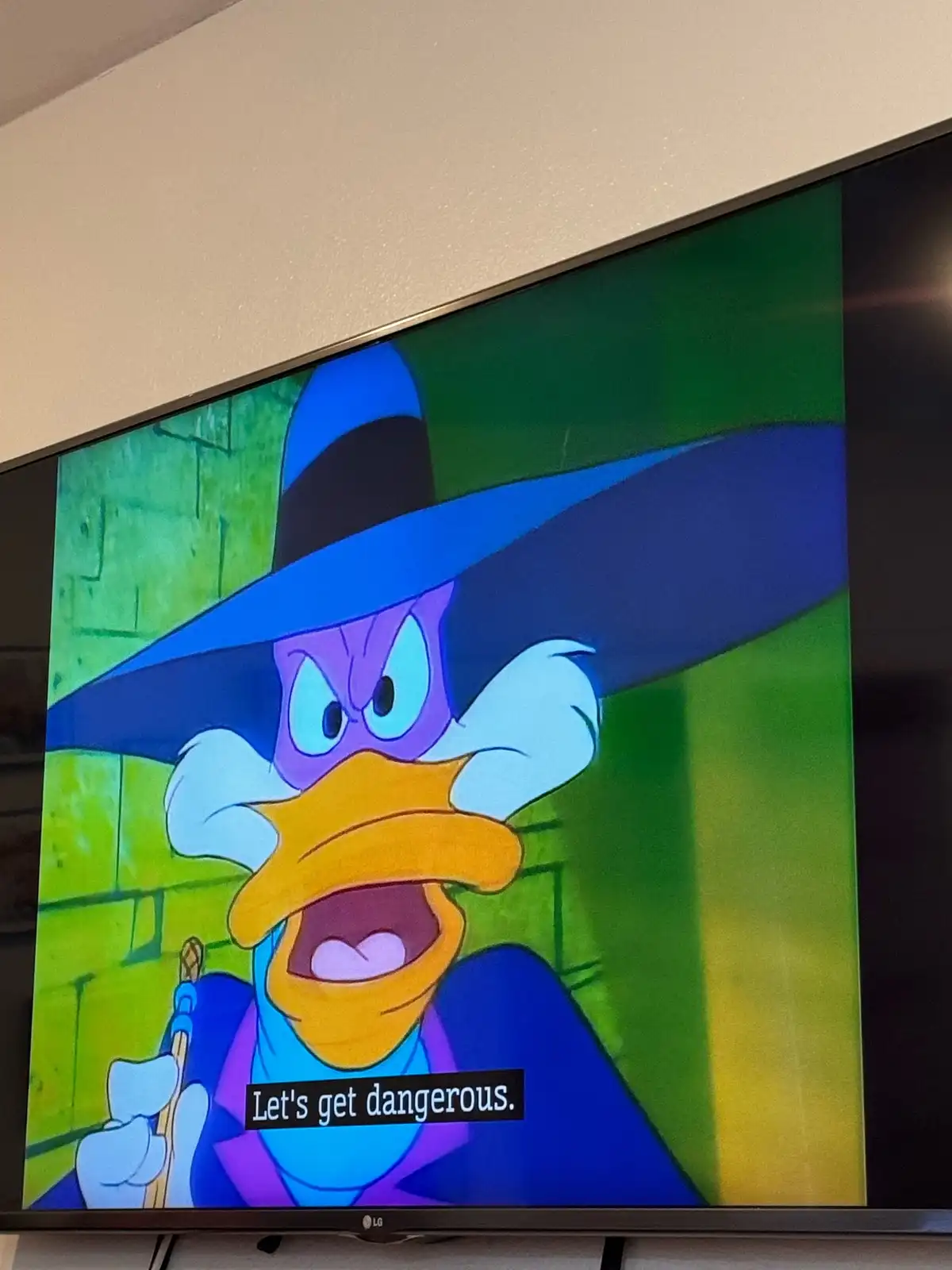 A TV screen displays an animated cartoon witch duck with a wide blue hat, purple skin, and an angry expression, holding a…