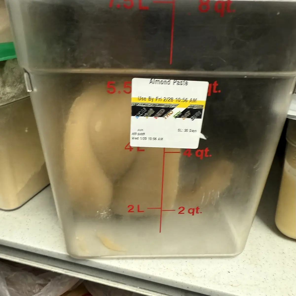A large, clear plastic container with red volume markings (2L, 4L, 5.5L) holds a beige, viscous substance shaped like a…