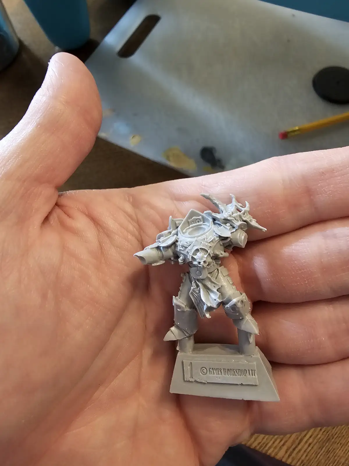 A person holds a small, unpainted grey plastic fantasy warrior miniature in their open palm, showing its intricate but…