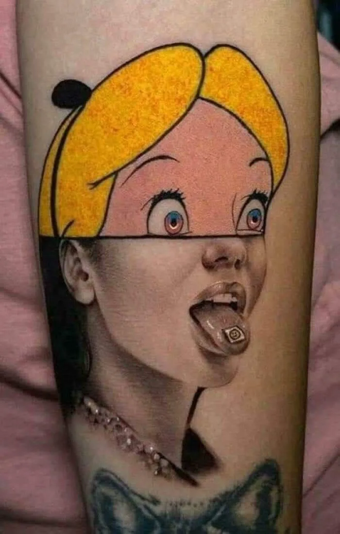 A tattoo on a person's arm depicts a split-face portrait: the top half is a cartoon-style Alice in Wonderland with yellow…