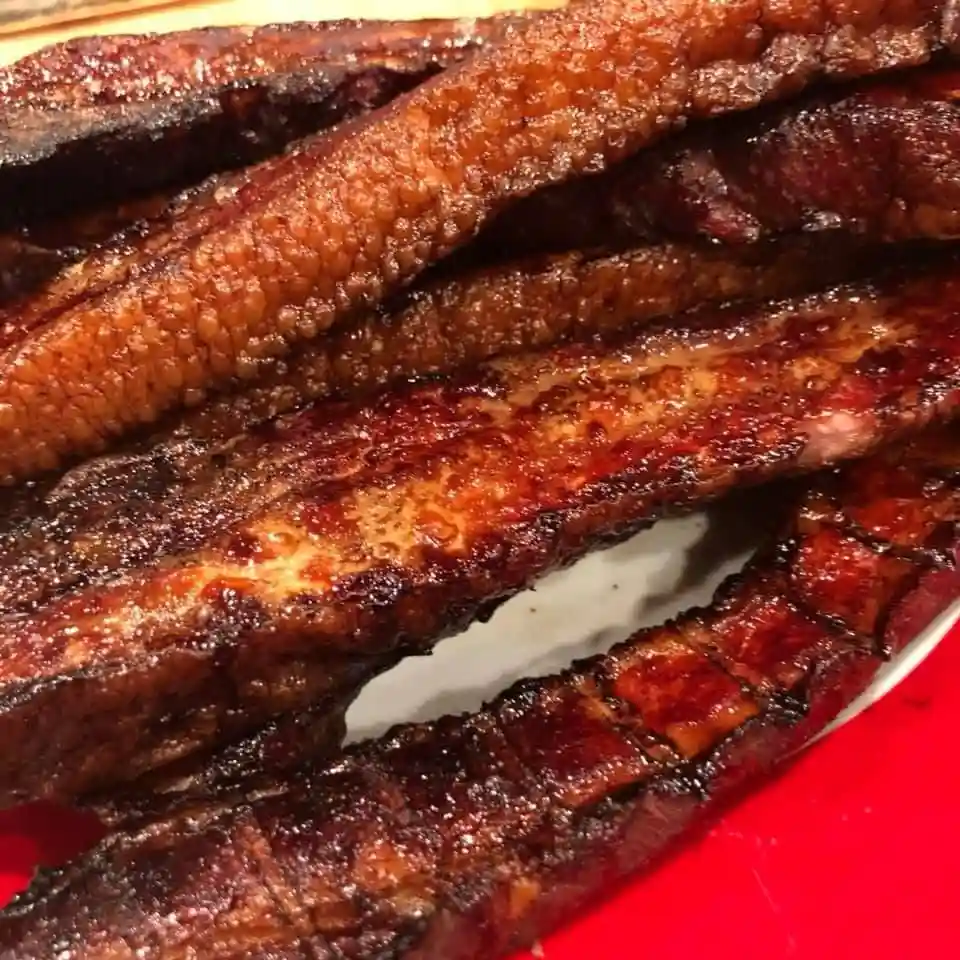 A close-up photo shows several strips of cooked, glazed meat with a dark, caramelized surface and visible bone structure…