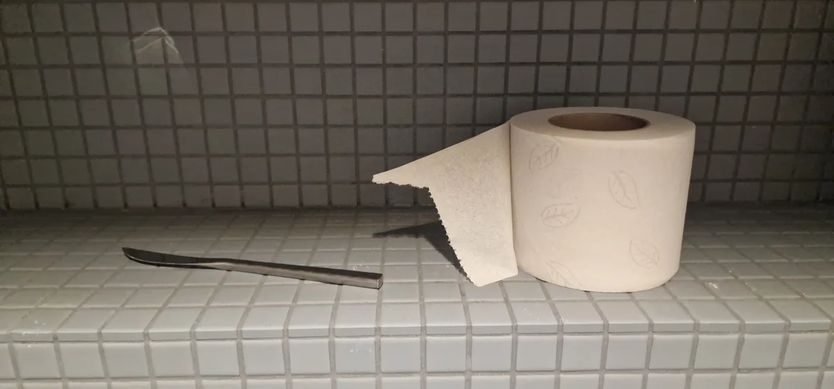 A toilet paper roll with a single sheet torn off sits on a tiled shelf next to a butter knife. The overlaid text reads 'i'm…