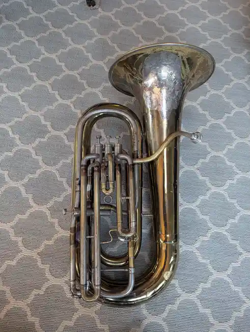 A brass euphonium rests on a grey and white patterned fabric surface. The instrument has a large bell, a complex array of…