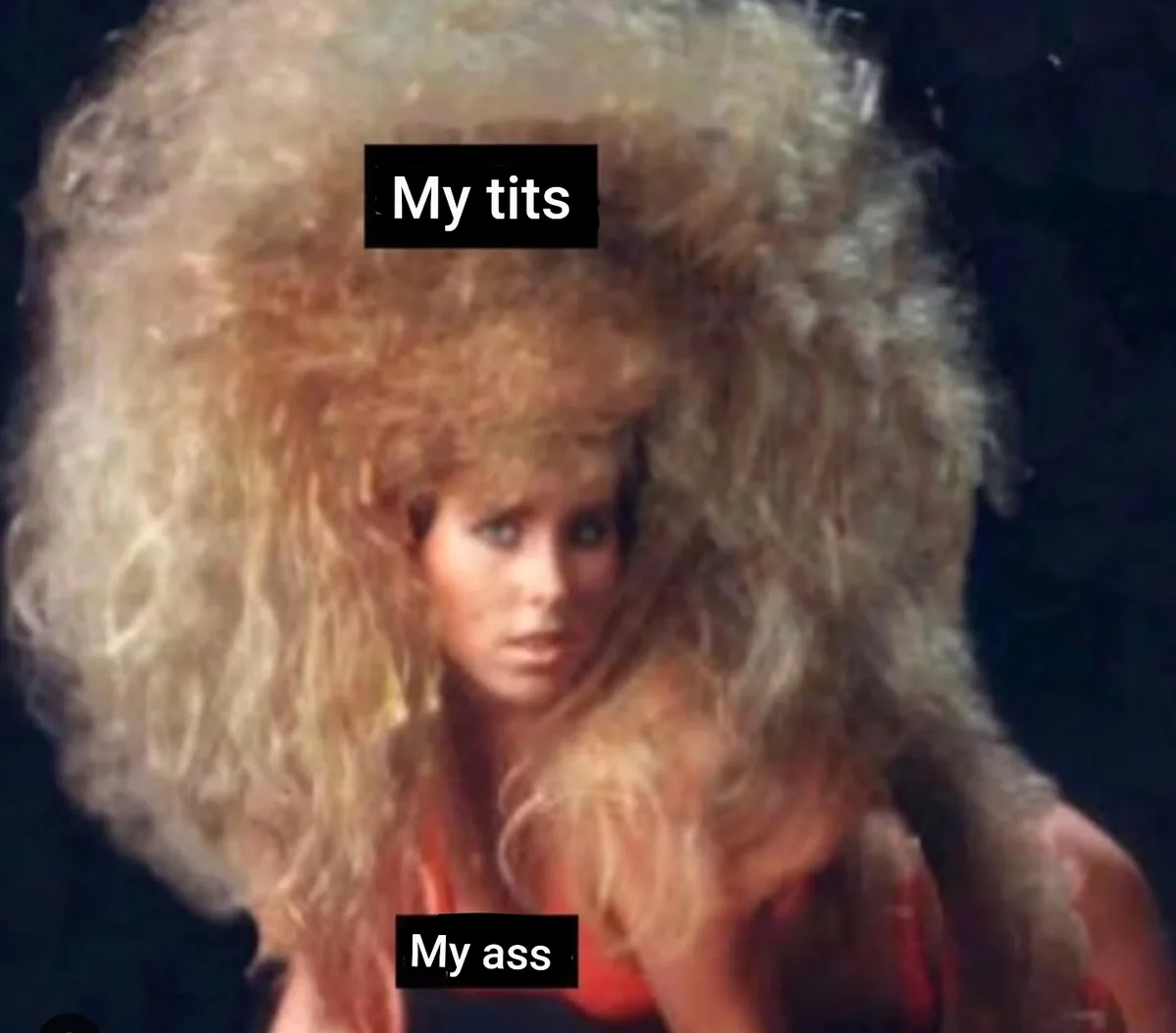 A woman with an extremely large, voluminous, curly blonde wig obscures most of her body. Two black text boxes are overlaid…