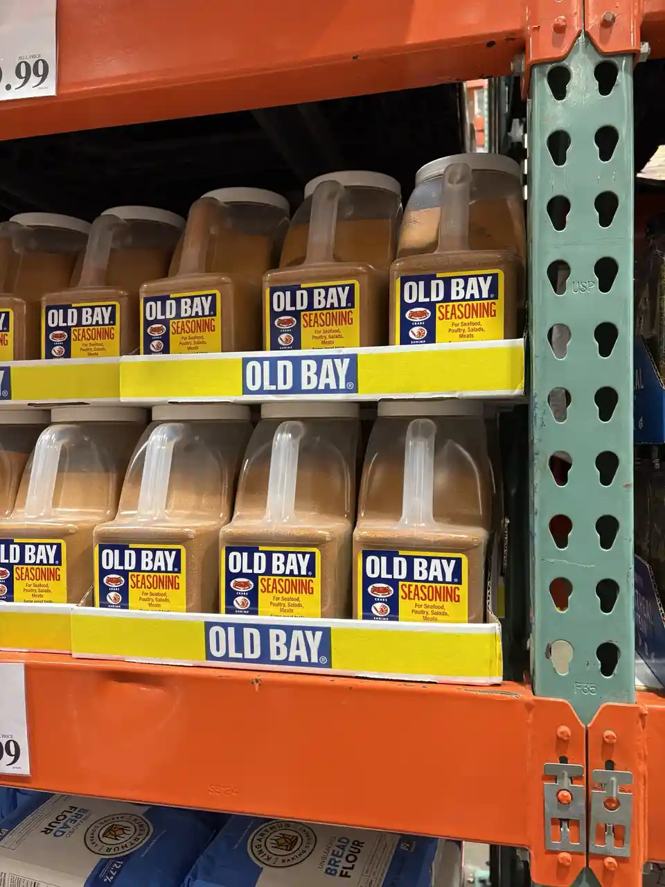 A close-up shot of multiple large, clear plastic containers of Old Bay Seasoning neatly arranged on orange and yellow…