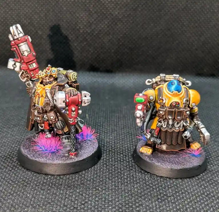 Two intricately painted miniature figurines, likely from a tabletop wargame, stand on circular bases against a dark textured…