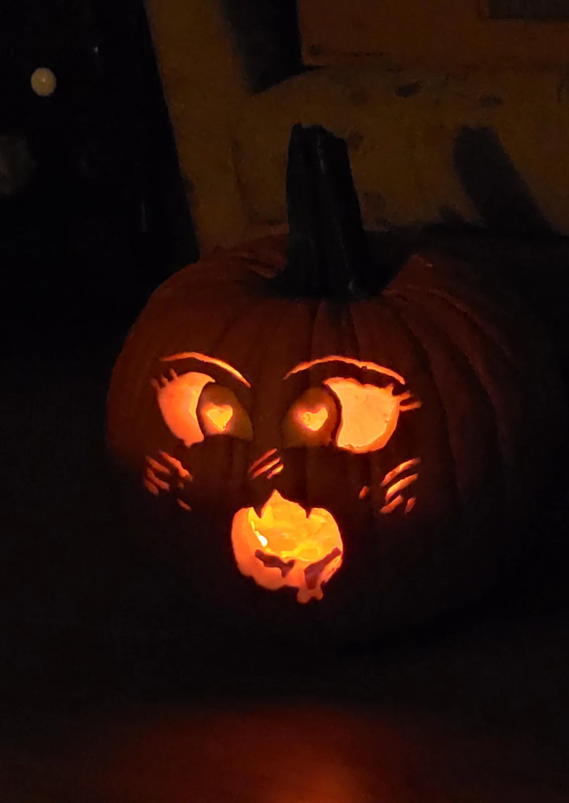 A close-up of a carved Halloween pumpkin illuminated from within, featuring large, expressive eyes with heart-shaped pupils…