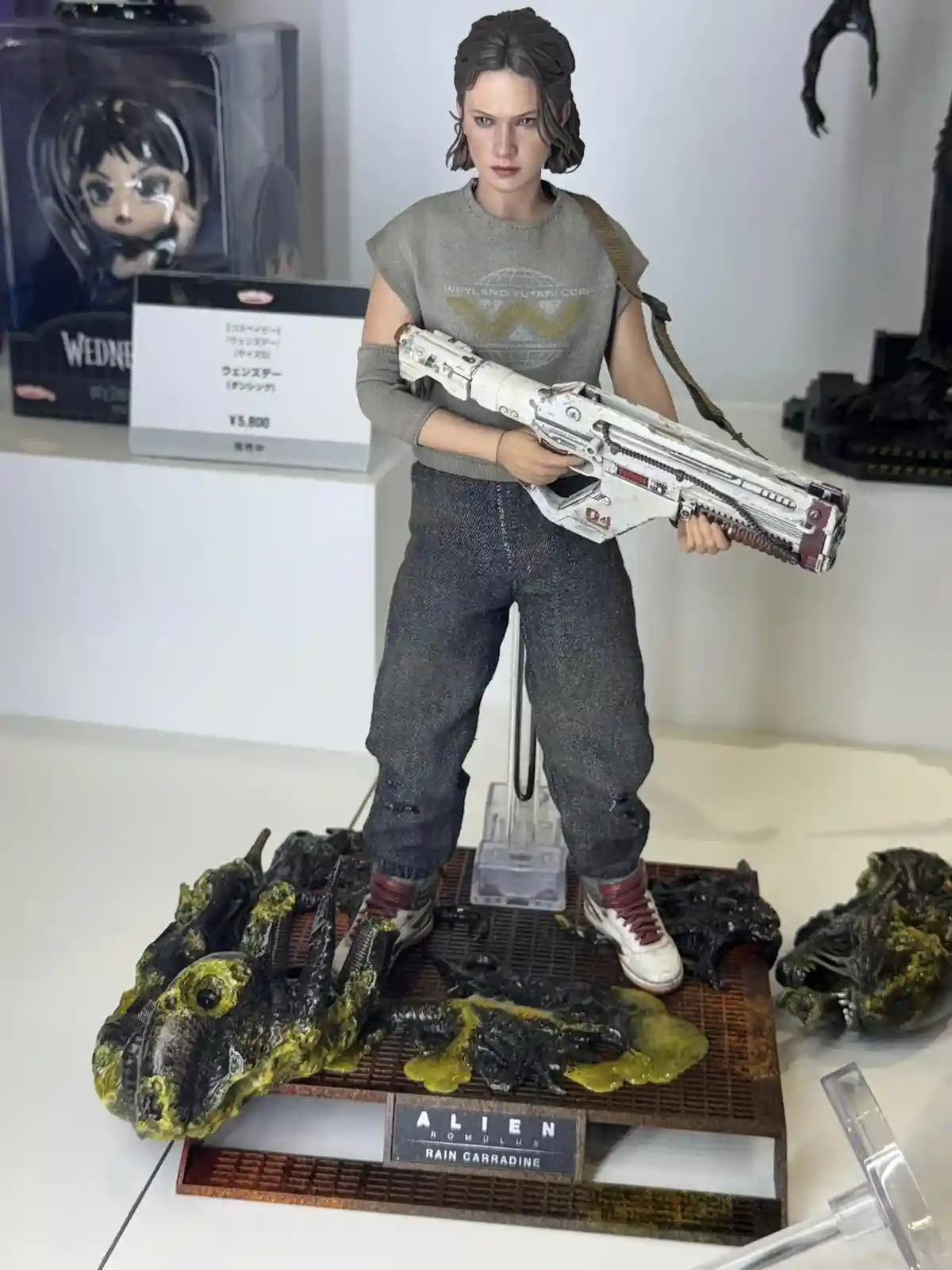 A highly detailed action figure of Rain Carradine from the movie 'Alien: Romulus' stands on a display base surrounded by…