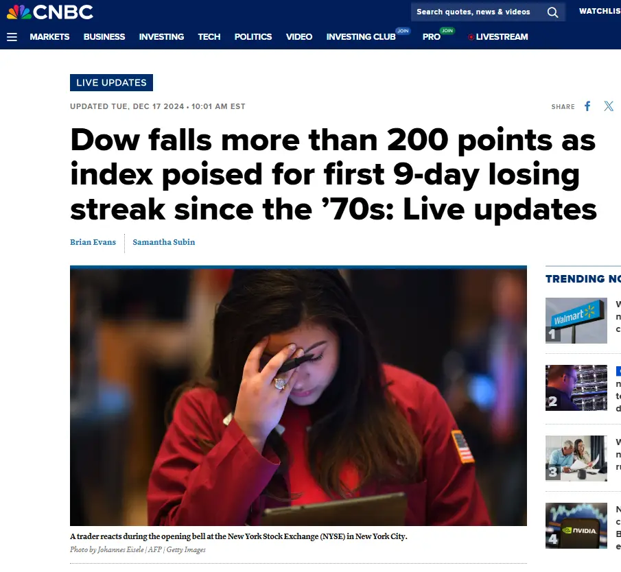 A screenshot of a CNBC news article shows a distressed female stock trader in a red jacket holding her head in her hand…