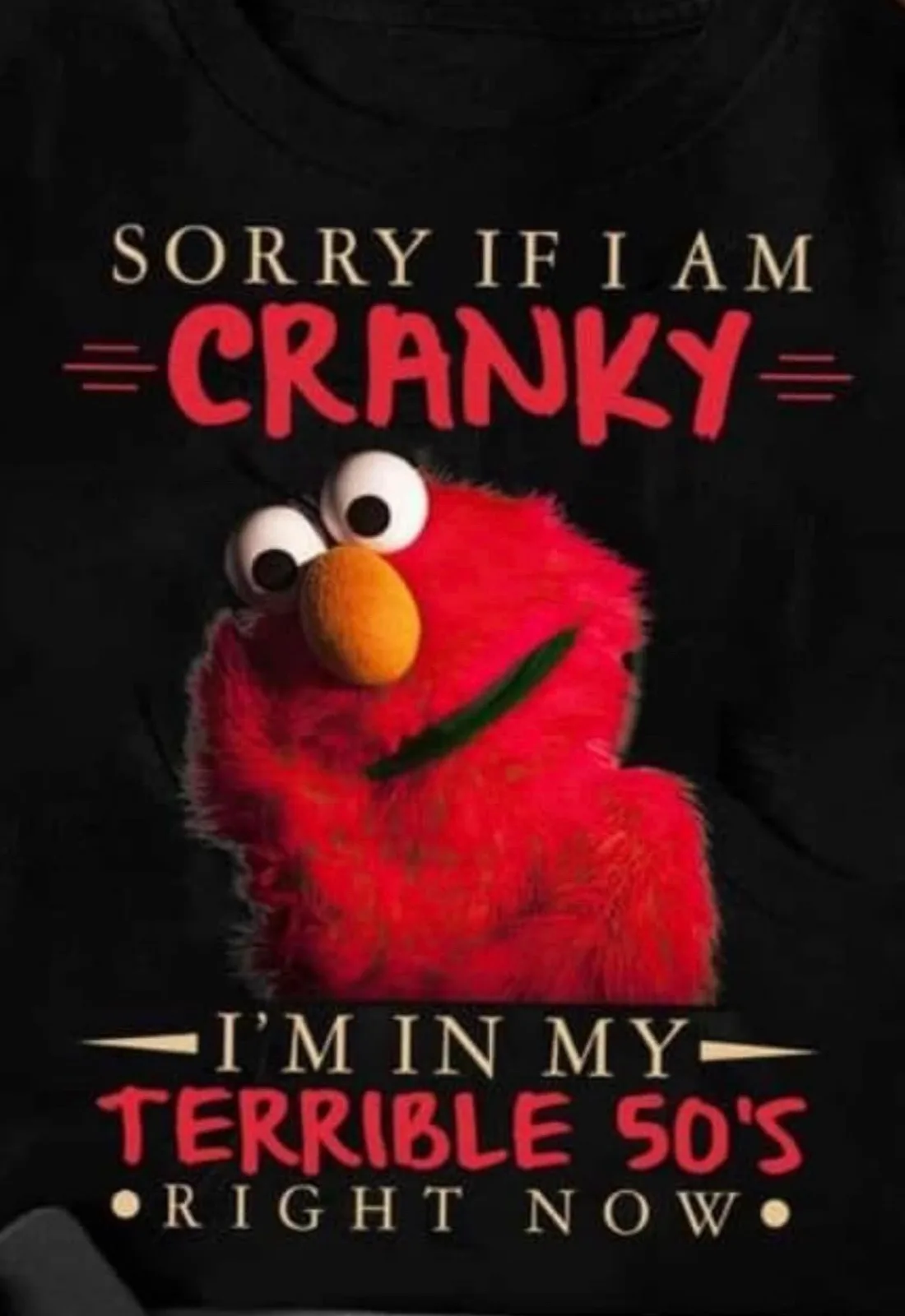 A black t-shirt features a photo of the red, furry Sesame Street character Elmo with a grumpy, annoyed expression. Above…