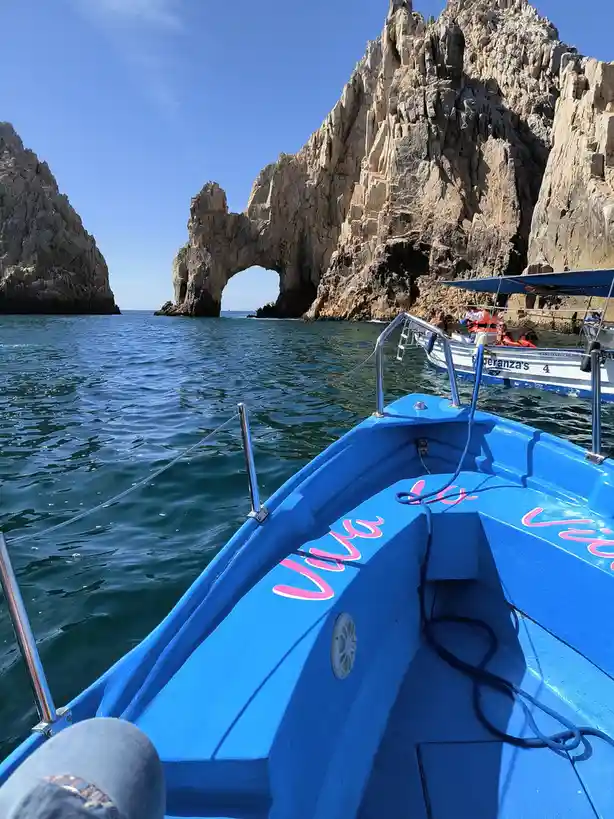 A first-person view from the bow of a bright blue tour boat with 'viva la vida' written in pink cursive on its side…