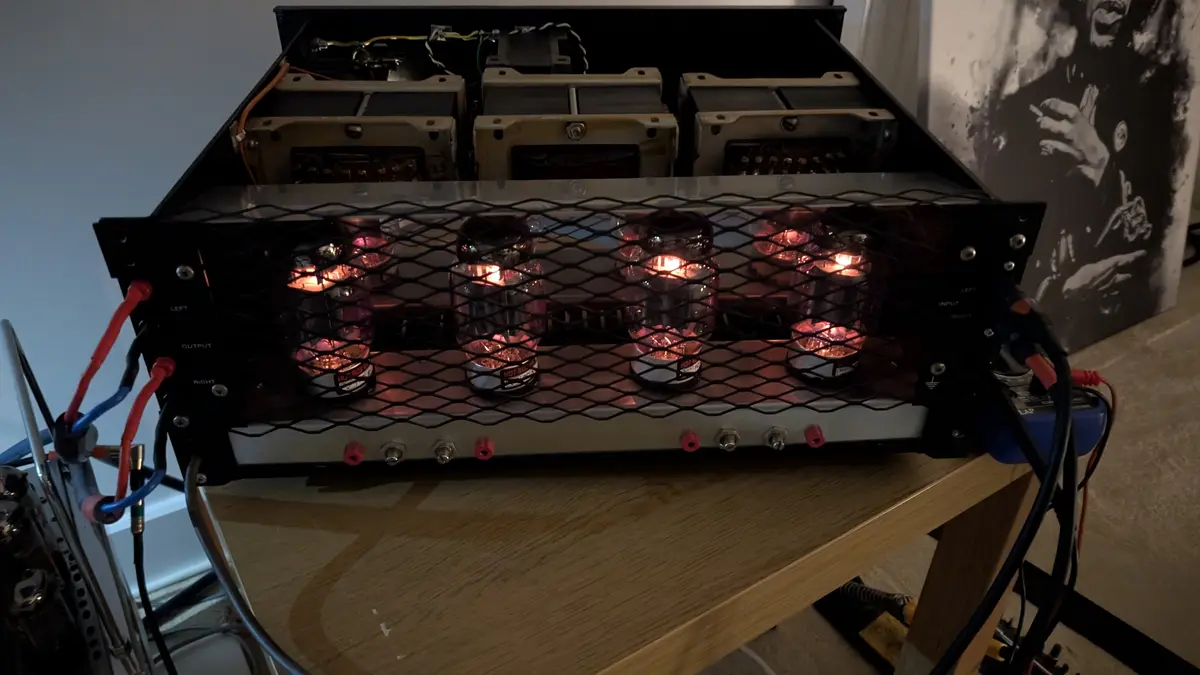 A close-up photo of an open tube amplifier with glowing vacuum tubes behind a black mesh grille, labeled 'HOT ROCKS' on each…