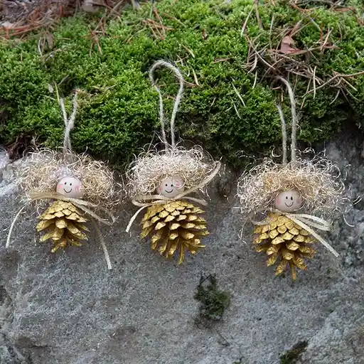 Three handmade pinecone ornaments, each shaped like a small angel with a painted smiling face, pink cheeks, and glittery…