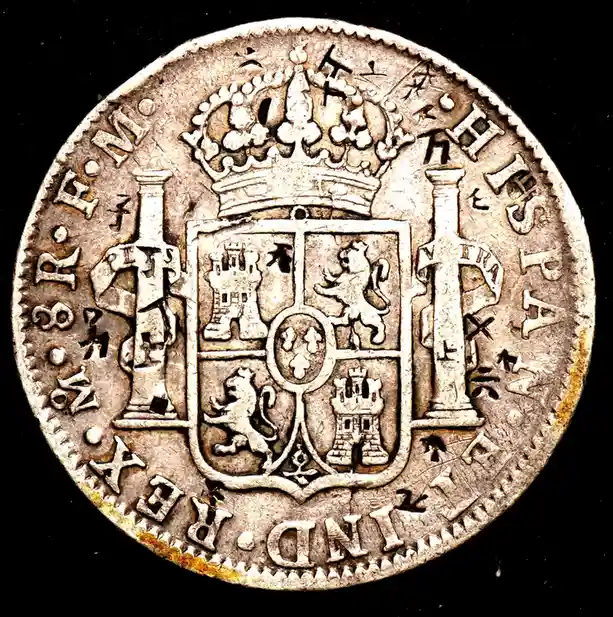 a close-up of an old silver coin showing a royal crest with a crown above a shield divided into four quarters—two with…