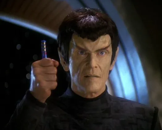 A still image of the Star Trek character Spock, played by Leonard Nimoy, holding a small blue and silver device in his right…