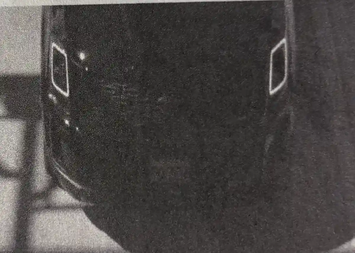 A grainy black-and-white photo shows the side of a dark-colored car with two white rectangular door handles visible. The…