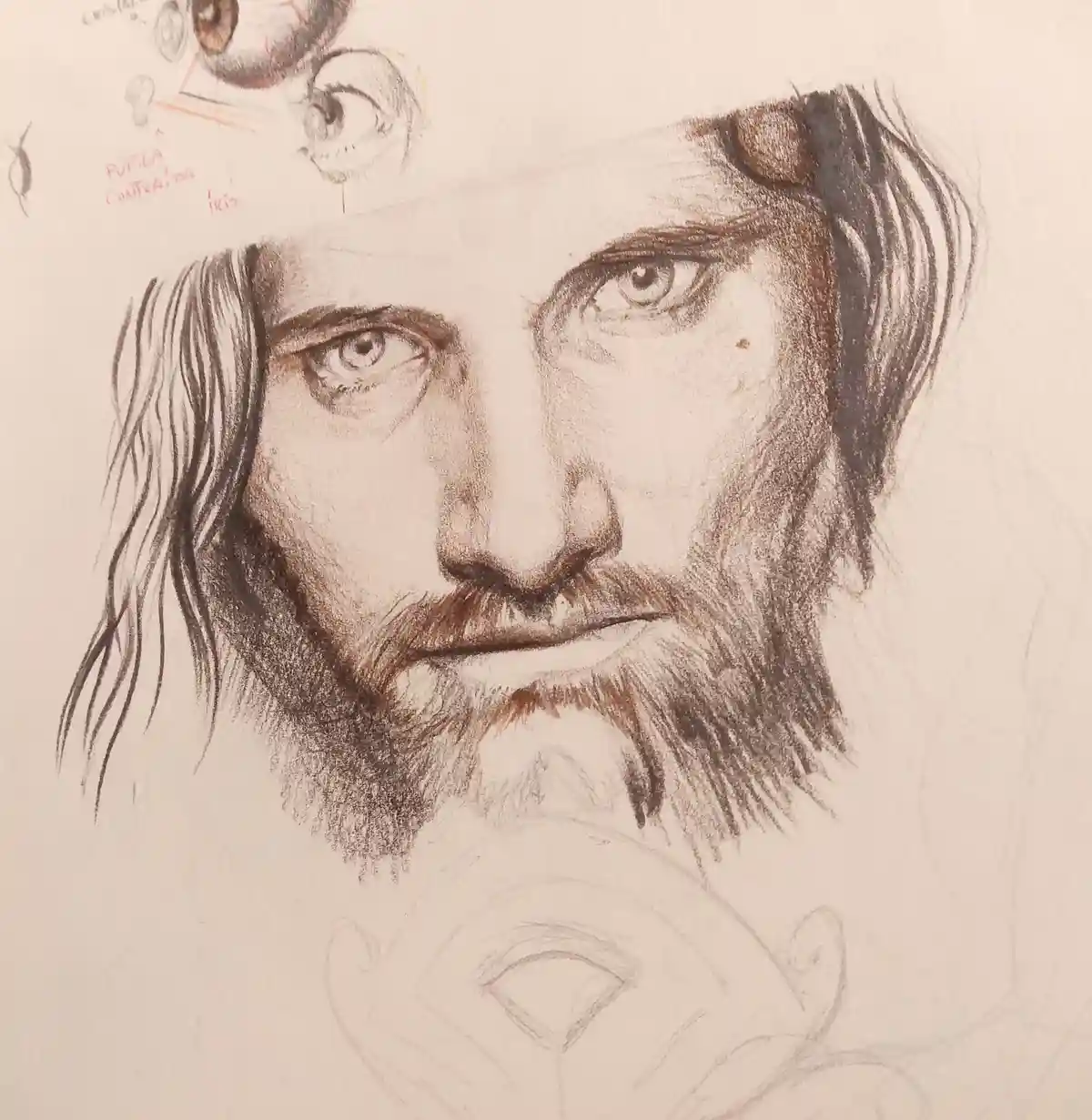 A detailed pencil sketch of a man's face with long hair and a beard, surrounded by rough eye-drawing sketches and…