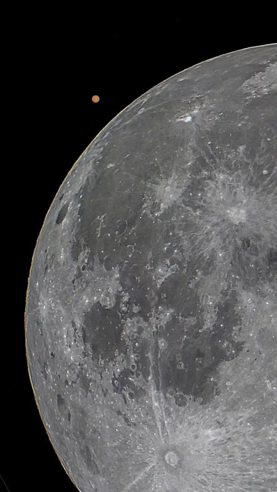 A close-up image of the moon's cratered gray surface against black space, with a small orange dot visible near the moon's…