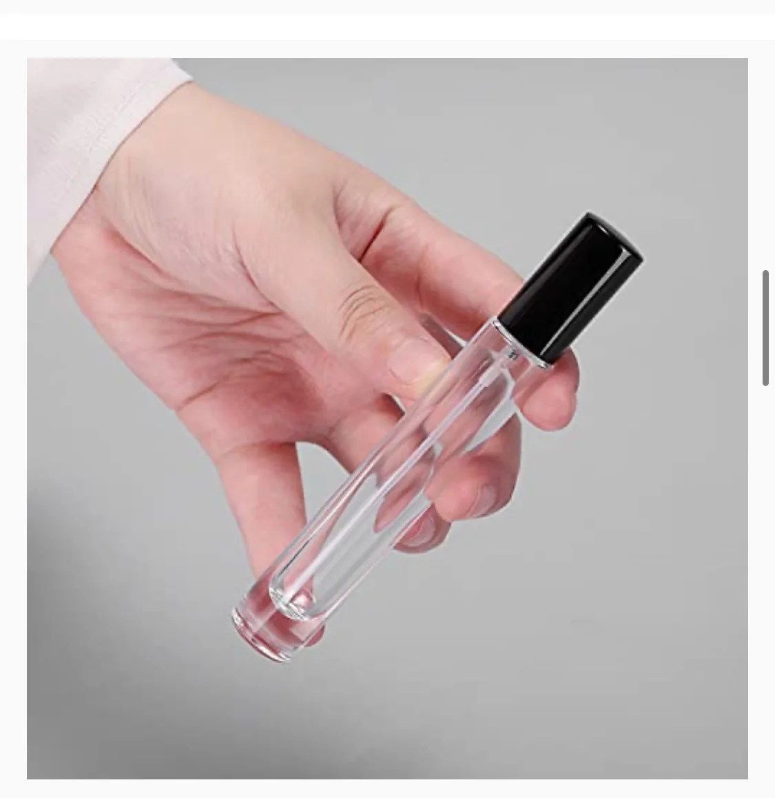 A hand holds a clear, empty rollerball perfume bottle with a black cap against a plain gray background. The overlaid text…