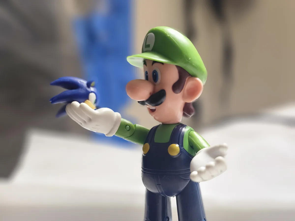 A plastic figurine of Luigi, recognizable by his green hat with an 'L', green shirt, and blue overalls, is holding a small…