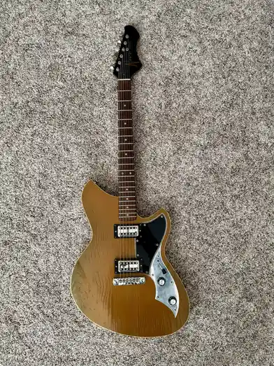 A light brown electric guitar with a black pickguard and chrome hardware lies flat on a gray carpet. The overlaid text reads…