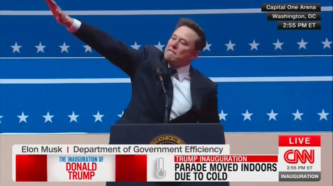 A man in a suit stands at a podium with a presidential seal, raising his right arm in a gesture resembling a political…