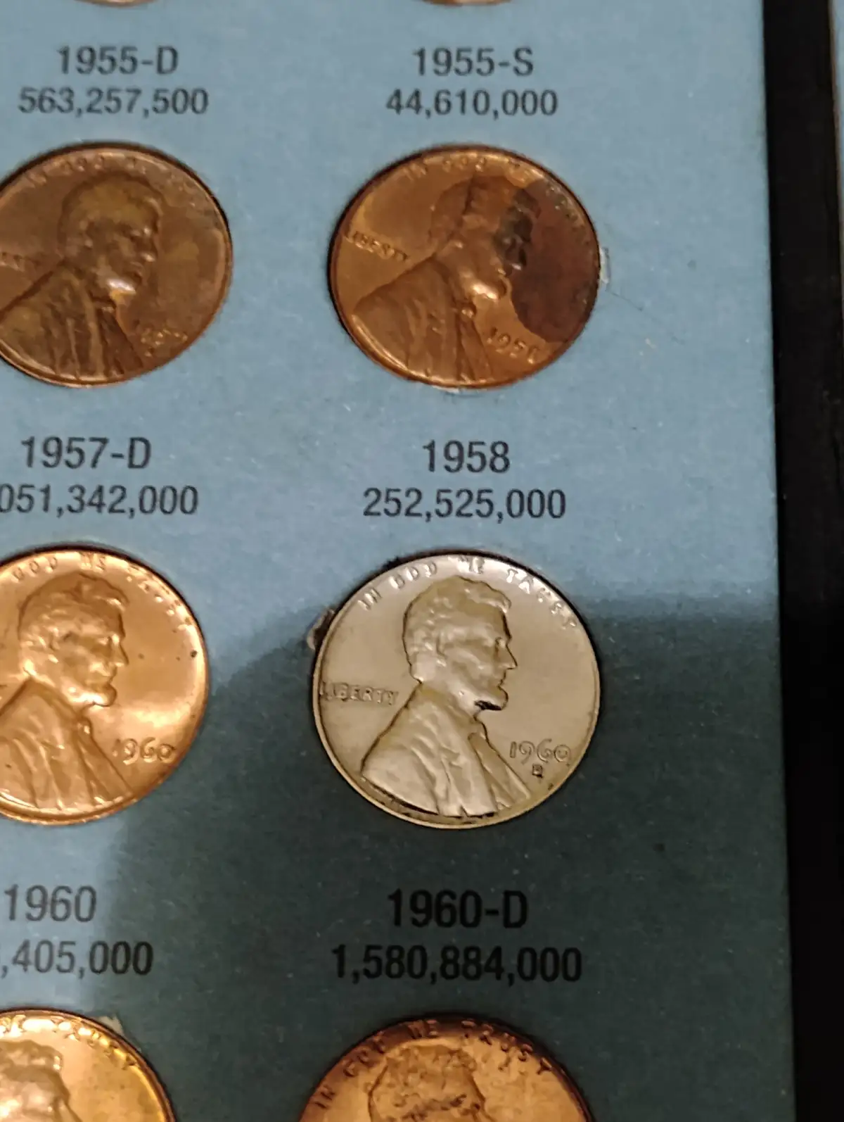 A close-up of a display showing U.S. Lincoln cents from 1955 to 1960, with their mintage numbers printed beside each coin…
