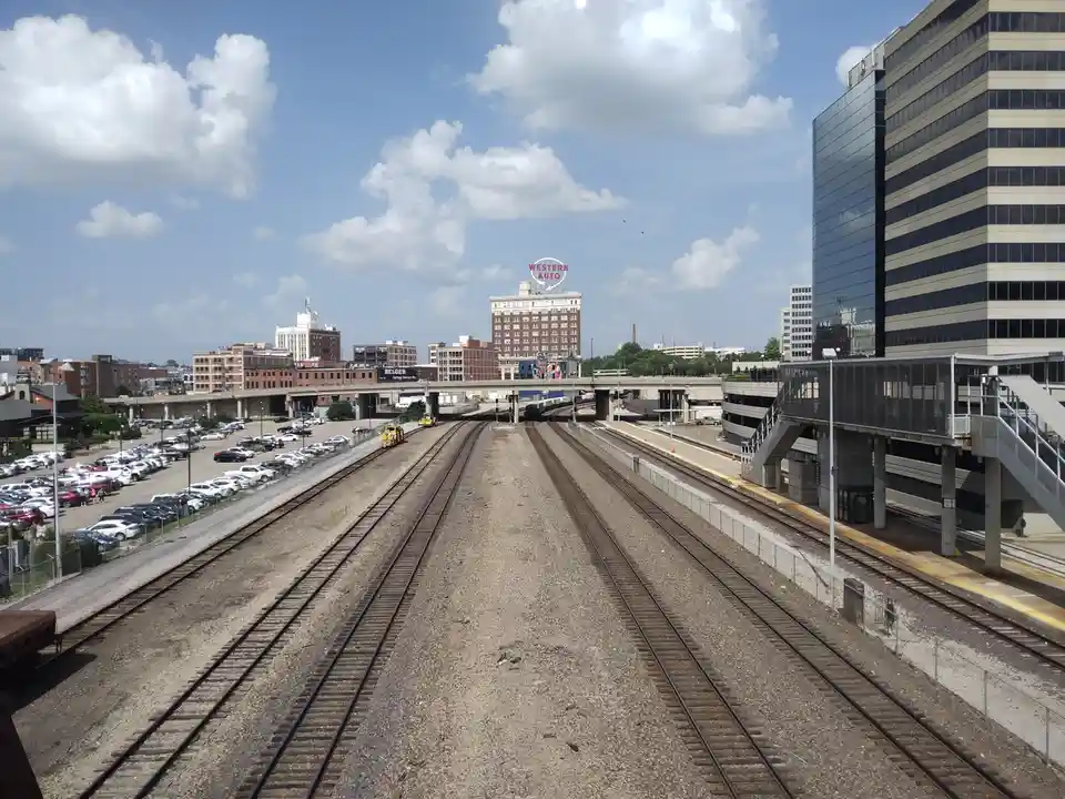 A wide-angle photo shows multiple train tracks converging toward a distant cityscape under a partly cloudy sky. On the right…