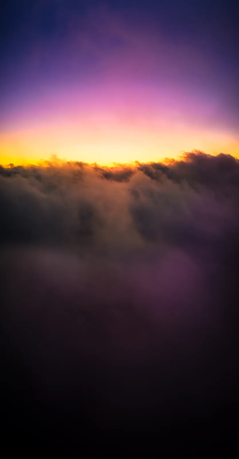 A serene photograph of a sunrise or sunset viewed from above a thick layer of clouds, with the sky transitioning from deep…
