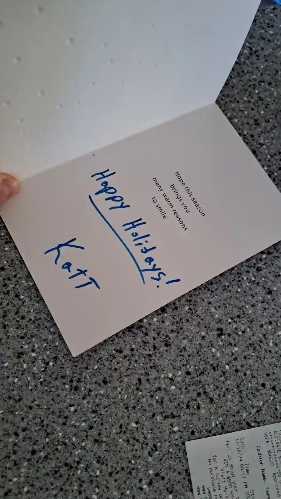 A close-up photo shows a person holding an open holiday card with printed text 'Hope this season brings you many warm…