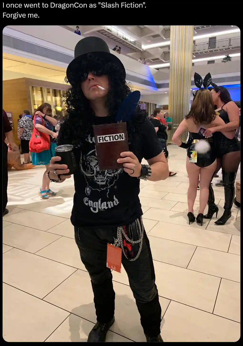 A person dressed as the musician Slash, complete with curly wig, top hat, sunglasses, and holding a book labeled 'FICTION'…