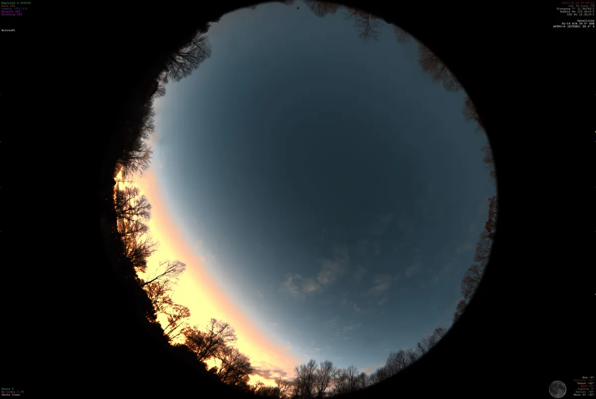A fisheye lens photo shows a circular view of a sunrise or sunset with silhouetted trees around the edge, overlaid with…