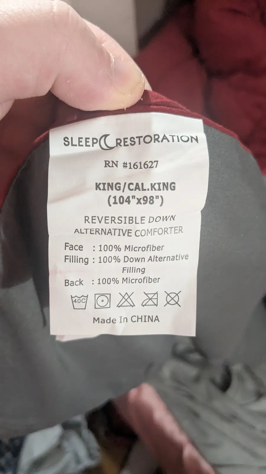 A close-up photo shows a hand holding a white fabric care label from a 'Sleep Restoration' comforter. The label details the…