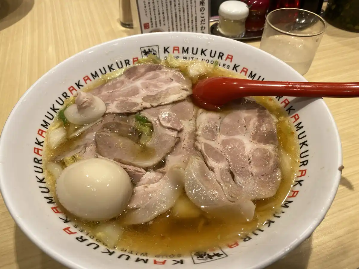 a close-up photo of a ramen bowl from the restaurant kamukura, featuring an exceptionally large portion of chashu pork, a…