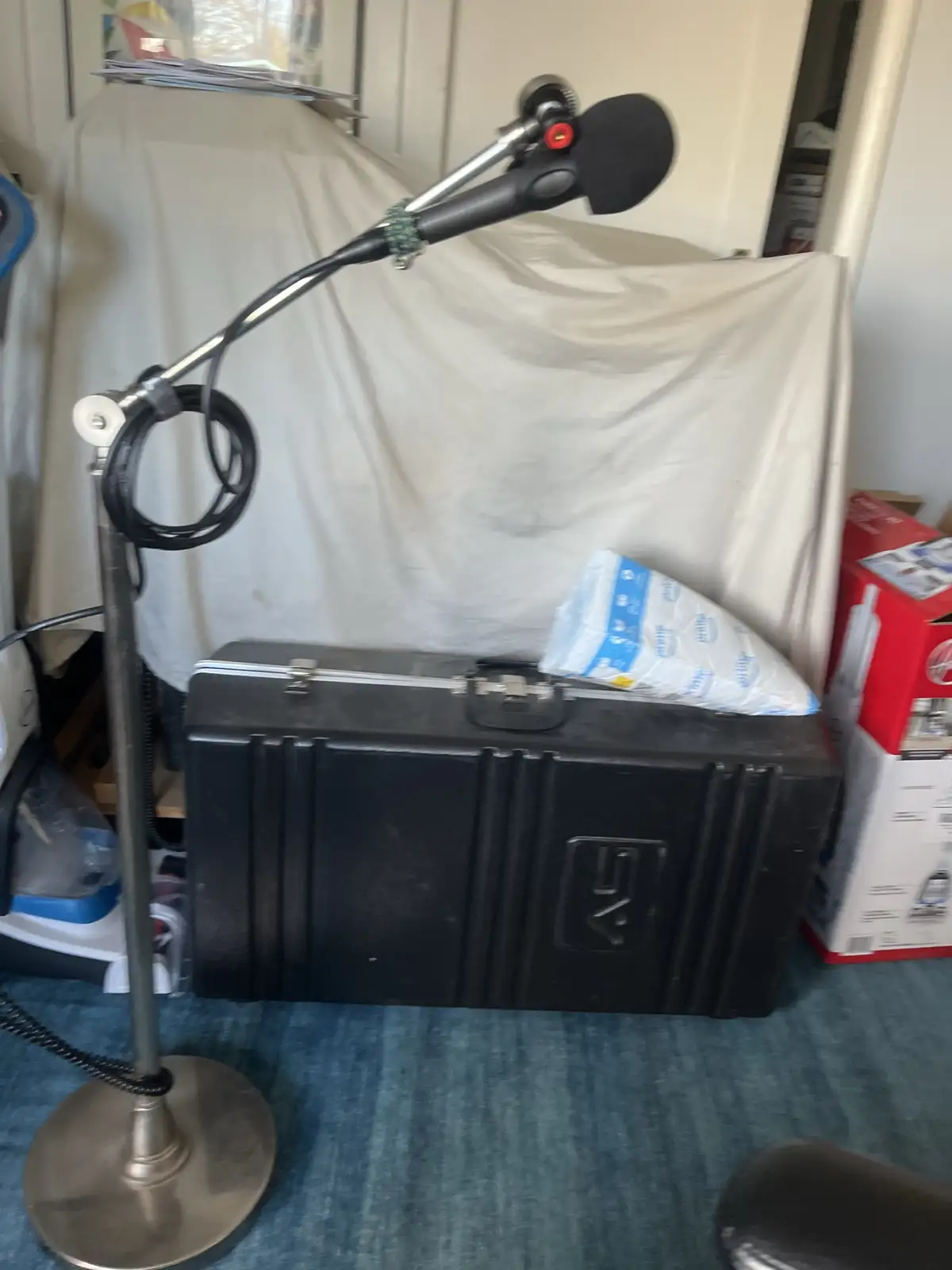 A microphone on a stand is positioned in front of a black hard case with a white cloth backdrop. A bag of what appears to be…