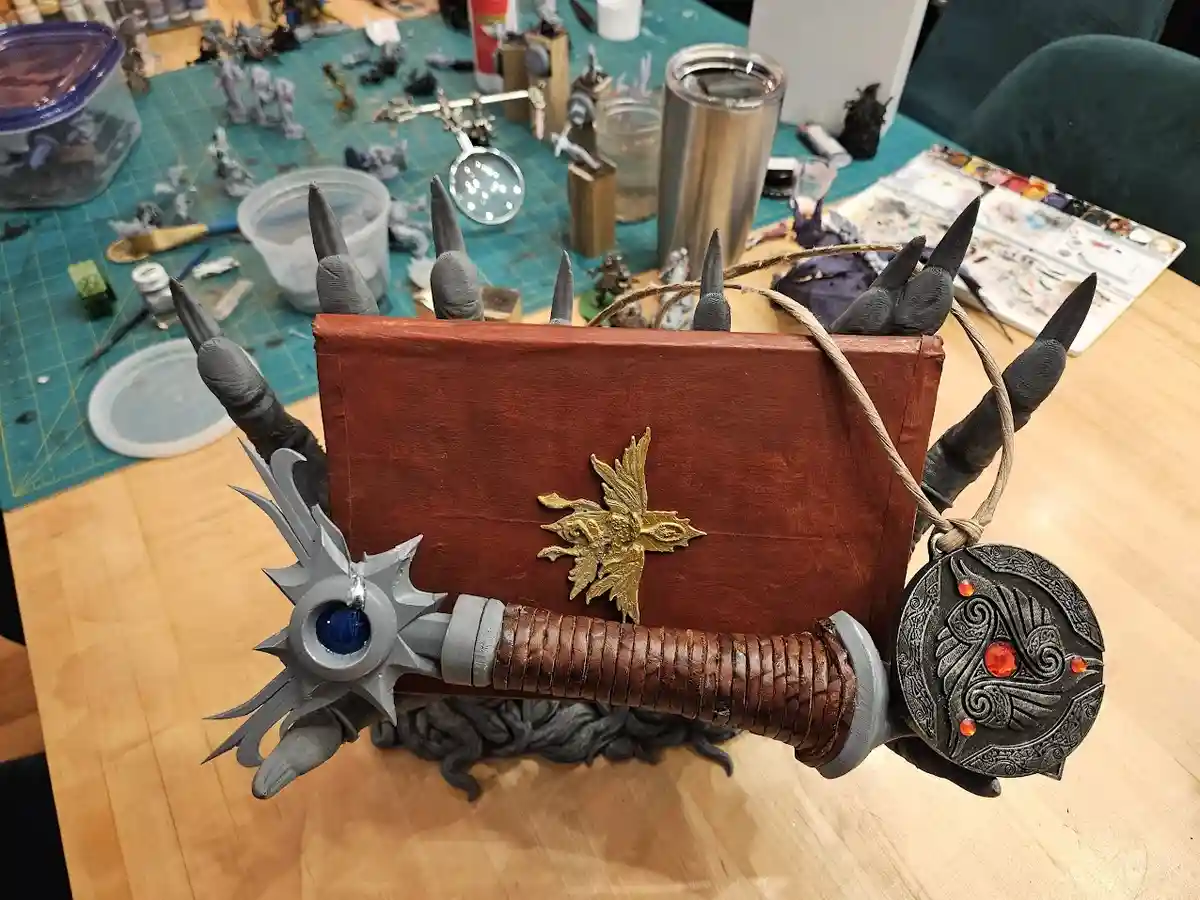 A highly detailed, custom-made sword is constructed from a brown leather-bound book, with spikes protruding from its spine…